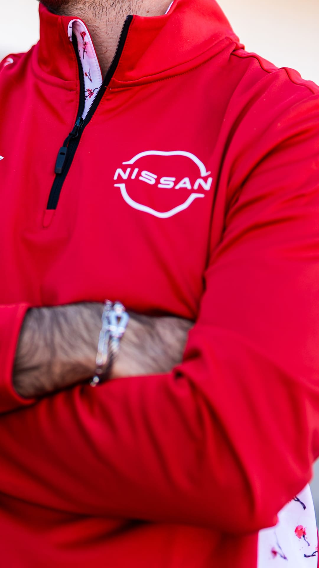 A close-up of a person wearing a bright red Reflo half-zip midlayer made for Nissan Formula E