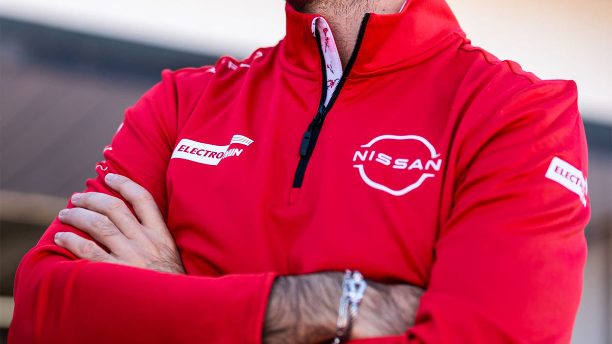 A close-up of a person wearing a bright red Reflo half-zip midlayer made for Nissan Formula E