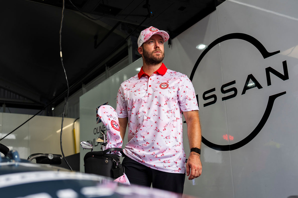 A man wearing Reflo's Sakura Golf Club clothing, standing in a Nissan race garage